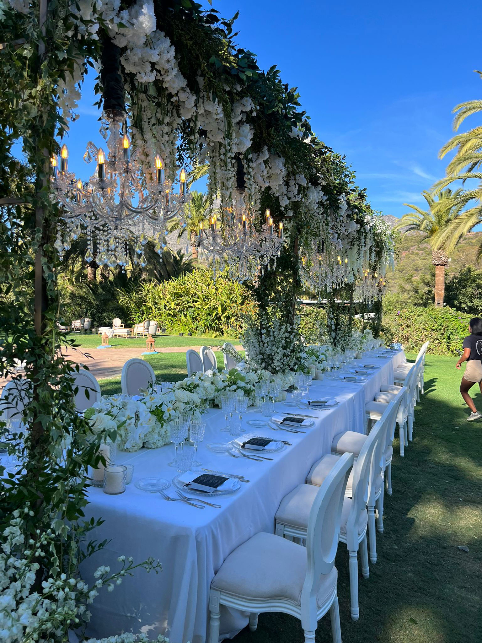 Mesa dos noivos com diversos vasinhos com flores de vários tamanhos e com bastante verde no arranjo aéreo